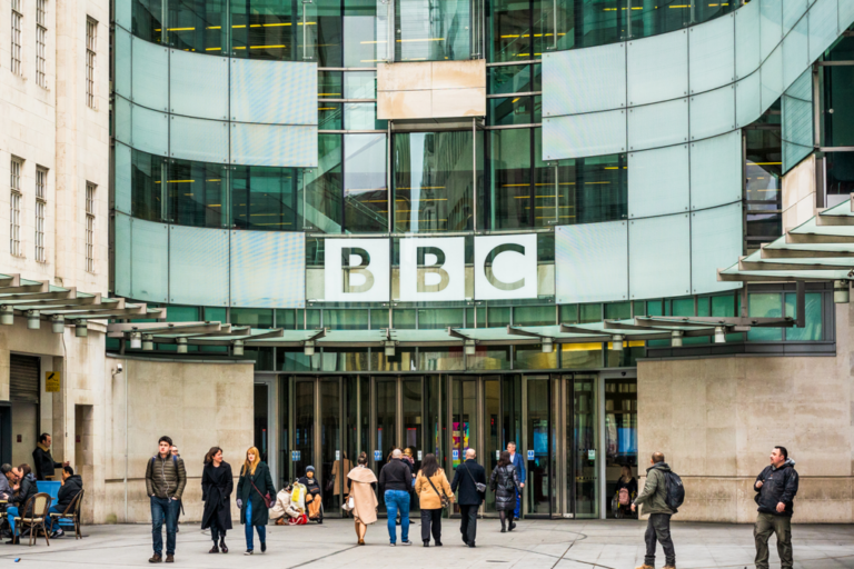 People walk in front of BBC Broadcasting House, a modern glass-fronted building with a large BBC sign above the doors, following the recent appointment of Deborah Turness.