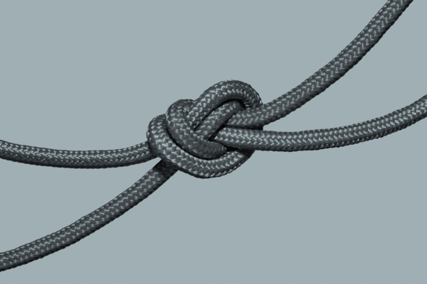 A close-up view of a simple overhand knot tied in a grey braided rope, symbolizing crisis communications, set against a plain light grey background.