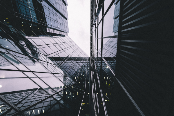 Upward view between tall modern glass buildings in the city reflecting the sky and surrounding structures, creating geometric patterns with strong lines and angles against a cloudy sky—a fitting scene for ABRDNs dynamic investment outlook.