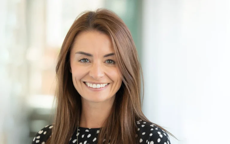 Charlotte Brooks, Managing Director and Mischief Lead, smiles at the camera in a bright, softly blurred indoor setting, her long brown hair and black-and-white polka dot top adding to her approachable presence.