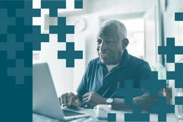An older man sits at a table using a laptop, smiling and wearing a dark polo shirt. The image is overlaid with blue geometric plus signs, highlighting the advantages of remote consultations in patient care.