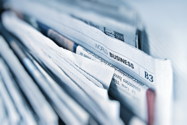 A close-up image of a stack of newspapers, with the top paper showing the section title World Business in bold letters, reflects media communication. The edges of the papers are slightly curled and overlapping.