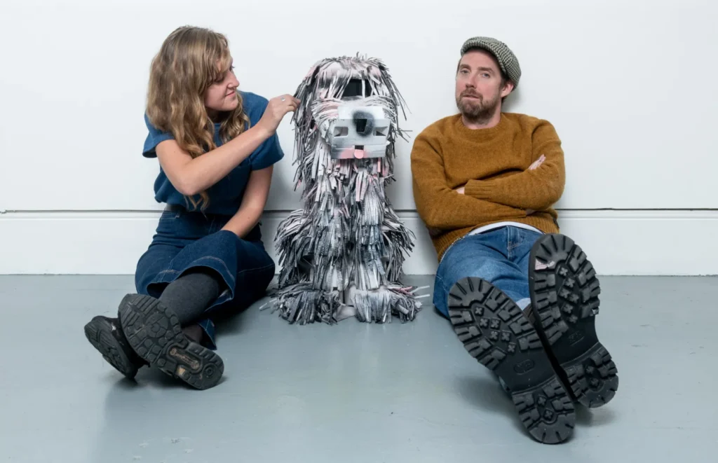 Two people sitting next to a paper sculpture