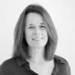 Black and white portrait of Alison Dunlop, a woman with shoulder-length hair, wearing a dark blouse and a small necklace, smiling gently at the camera against a plain light background.