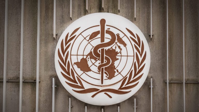 The WHO emblem, symbolizing medicine and global health, is mounted on a concrete wall—a reminder of the organizations commitment to fighting non-communicable diseases (NCDs) worldwide.