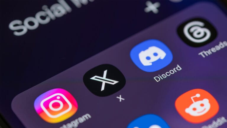 A smartphone screen displays social media app icons, including Instagram, X news (formerly Twitter), Discord, Threads, and Reddit, on a dark background.