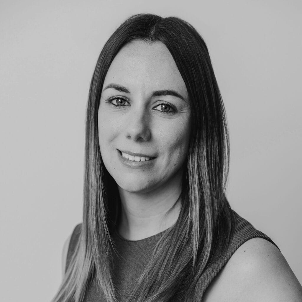 Black and white portrait of Hannah Slater, a woman with straight, shoulder-length hair, wearing a sleeveless top, smiling gently, and looking into the camera against a plain background.