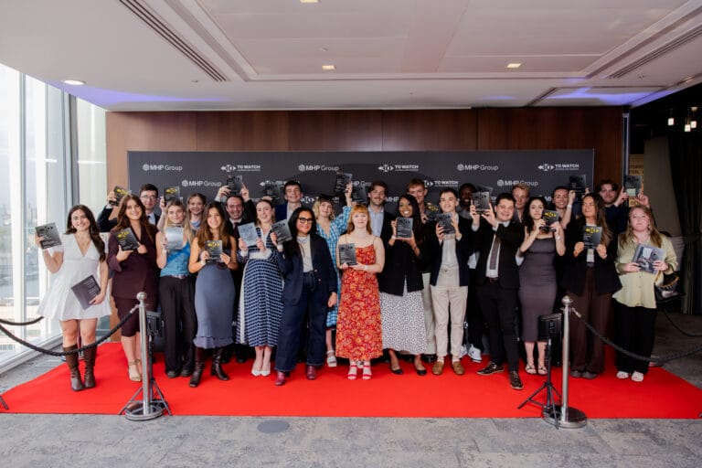 A large group of people, including rising media stars, stand on a red carpet, posing and holding Journalism Awards in front of a black backdrop with logos. The group is dressed in formal and semi-formal attire, smiling for the camera.