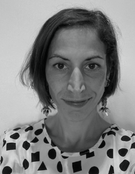 Black and white portrait of Camilla Zucchi, a woman with short, straight hair, wearing earrings and a patterned top with black geometric shapes on a light background, looking directly at the camera with a neutral expression.