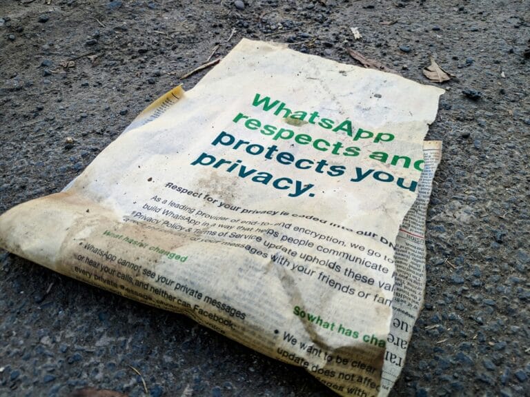 A dirty, crumpled paper with WhatsApp privacy in bold green text lies discarded on a rough, gravelly ground—a stark reminder of the privacy paradox surrounding Meta’s promises. The paper looks weathered and neglected.