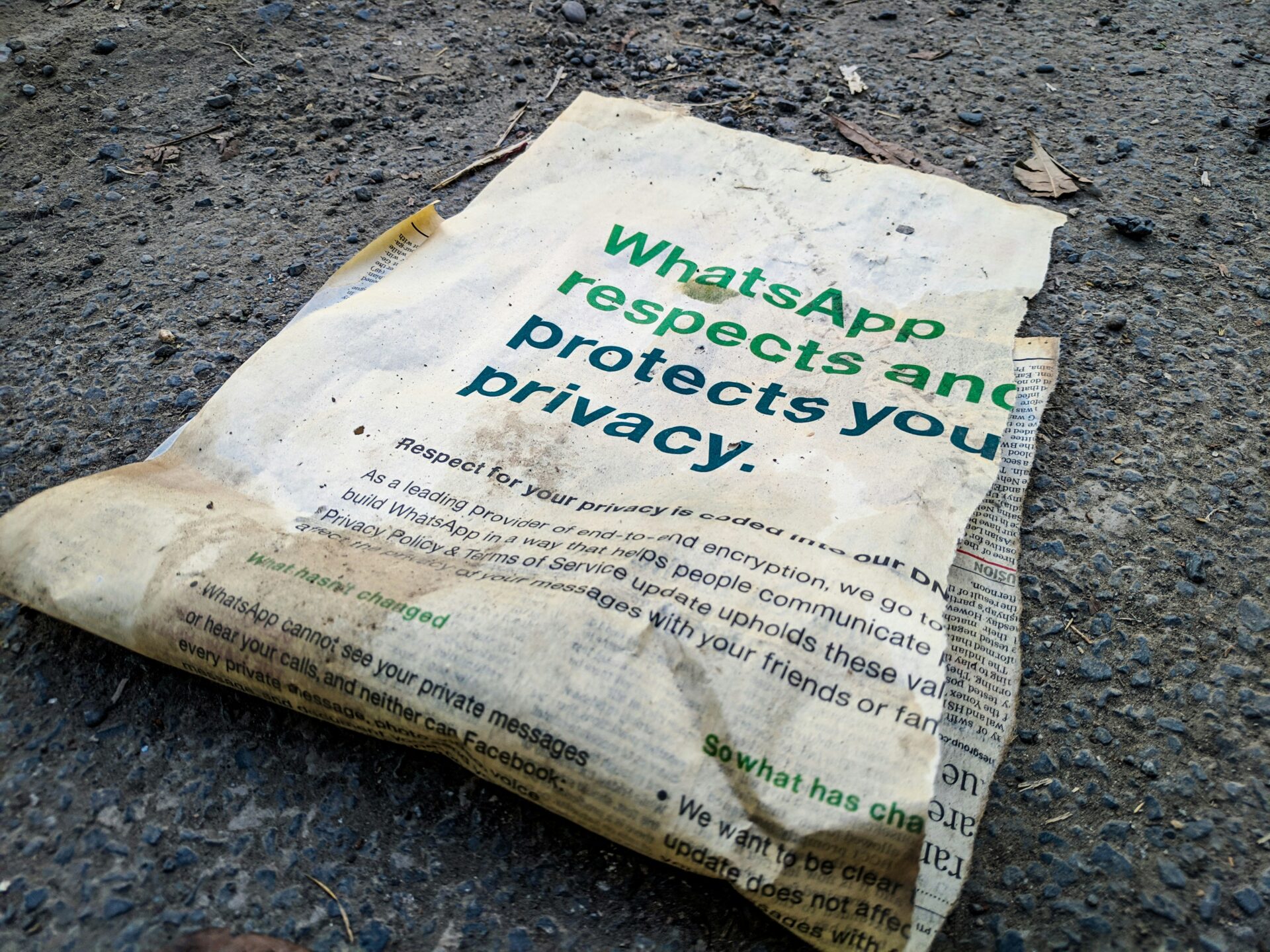 A dirty, crumpled paper with WhatsApp privacy in bold green text lies discarded on a rough, gravelly ground—a stark reminder of the privacy paradox surrounding Meta’s promises. The paper looks weathered and neglected.